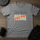 Stop Being Average T-Shirt on a gray fabric background with workout gear, promoting motivation and fitness.