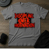 Discipline Over Motivation T-Shirt in gray color with bold red lettering on a wooden surface.